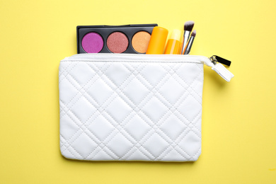 Bag with hygienic lipsticks and cosmetic products on yellow background, flat lay