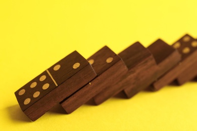 Falling wooden domino tiles on yellow background, closeup