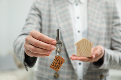 Real estate agent holding house figure and key indoors, closeup