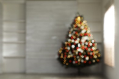Blurred view of beautifully decorated Christmas tree in empty room, space for text. Bokeh effect