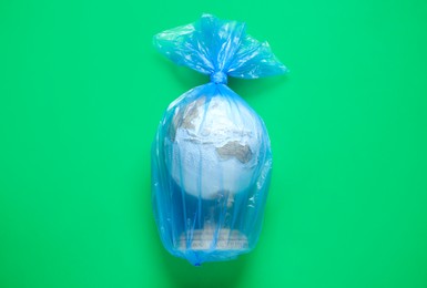 Photo of Globe in plastic bag on light green background, top view. Environmental conservation