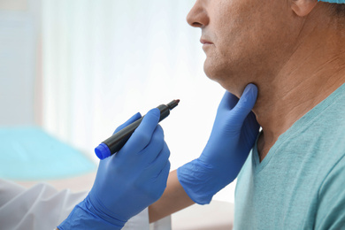 Photo of Surgeon with marker preparing man for operation in clinic, closeup. Double chin removal