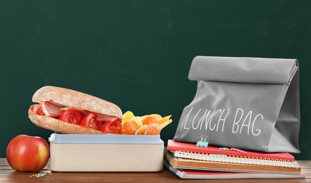 Lunch box with appetizing food and bag on wooden table near green chalkboard