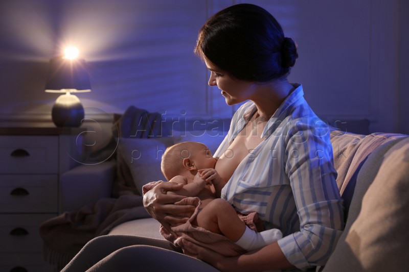 Photo of Young woman breastfeeding her little baby indoors at night