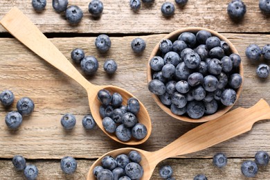 Spoons and bowl with tasty fresh blueberries on wooden table, flat lay