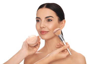 Professional makeup artist applying powder onto beautiful young woman's face with brush on white background