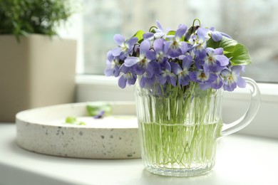 Beautiful wood violets in glass cup on window sill indoors, space for text. Spring flowers