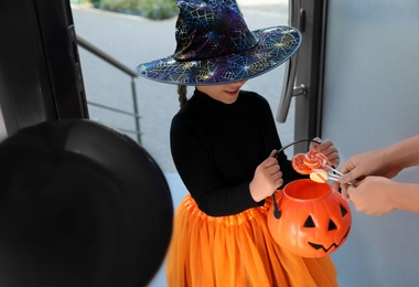 Cute little girl dressed as witch trick-or-treating at doorway. Halloween tradition