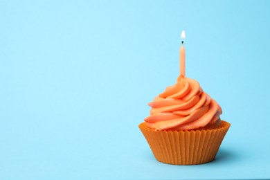 Photo of Delicious birthday cupcake with orange cream and burning candle on light blue background. Space for text