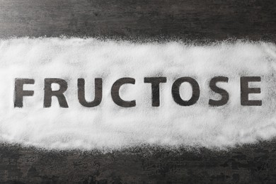 Word Fructose made of sugar on black table, top view