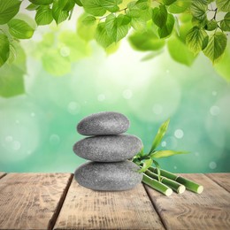 Stacked stones and bamboo stems on wooden table under green leaves against blurred background. Zen concept