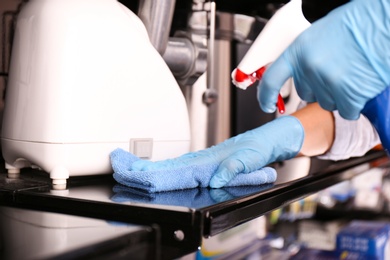 Woman cleaning shelf with rag and detergent in electronic store, closeup