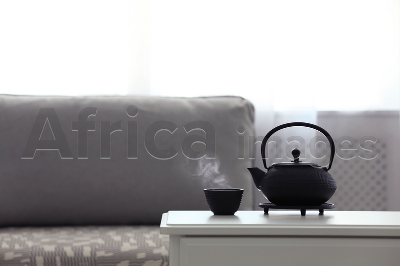 Teapot and cup of fresh hot tea on white table against blurred background. Space for text