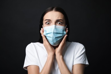 Young woman with protective mask feeling fear on black background