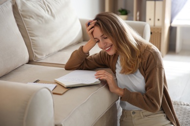 Happy woman writing letter on sofa at home