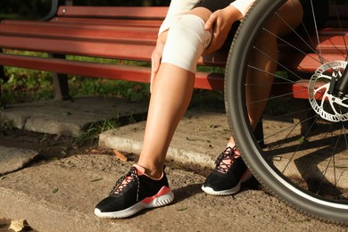 Woman with injured knee on wooden bench near bicycle outdoors, closeup