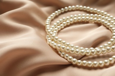 Elegant necklace with pearls on beige silk, closeup. Space for text