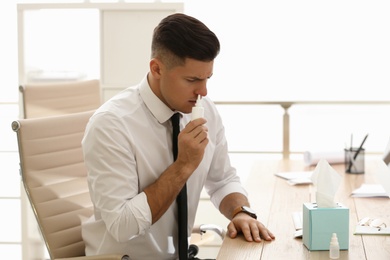 Ill businessman using nasal spray at table in office