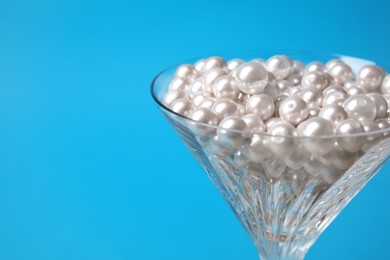 Photo of Beautiful martini glass with pearls on light blue background, closeup. Space for text