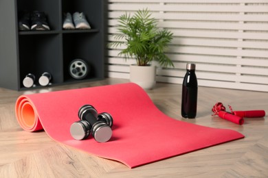Exercise mat, dumbbells, bottle of water and skipping rope on wooden floor indoors