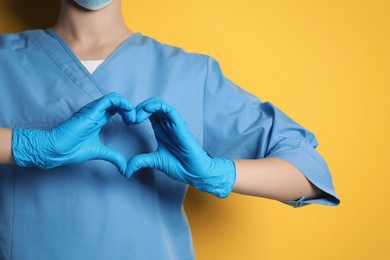 Photo of Doctor making heart with hands on yellow background, closeup