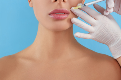 Woman getting lip injection on light blue background, closeup