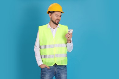 Photo of Male industrial engineer in uniform with phone on light blue background