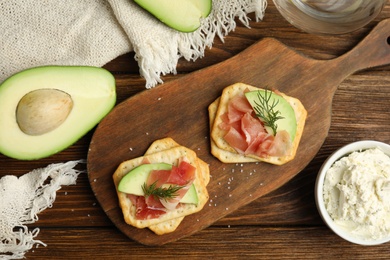 Delicious crackers with avocado, prosciutto and dill on wooden table, flat lay