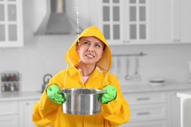 Young woman in raincoat collecting leaking water from ceiling at home. Time to call roof repair service