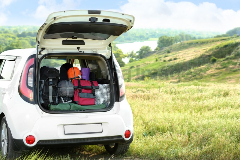 Car with camping equipment in trunk on green field. Space for text