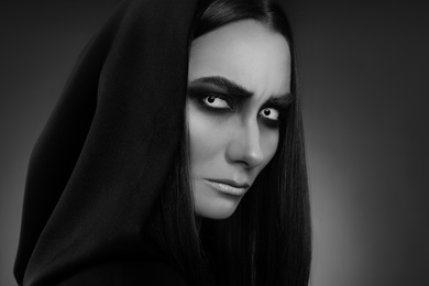 Mysterious witch with spooky eyes on dark background, closeup. Black and white effect
