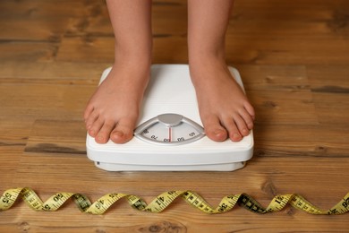 Photo of Overweight girl using scales near measuring tape on wooden floor, closeup