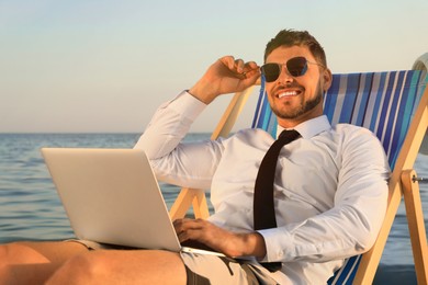 Photo of Happy man with laptop on deckchair near sea. Business trip