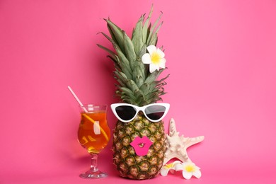 Photo of Funny pineapple with cocktail, plumeria flowers and starfish on pink background. Creative concept