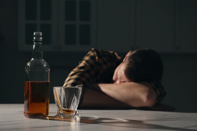 Addicted man sleeping at table in kitchen, focus on alcoholic drink. Space for text