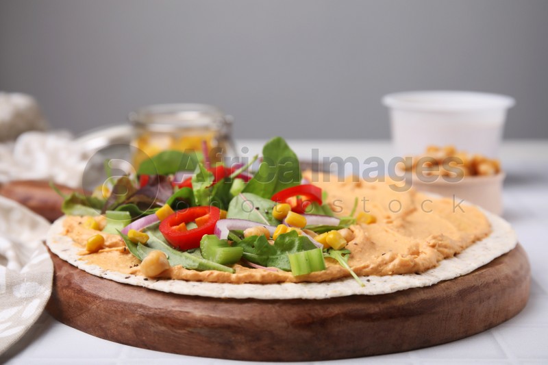 Photo of Tortilla with hummus and vegetables on table, closeup