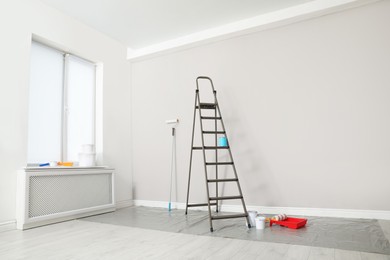 Decorator's tools and ladder near white wall indoors