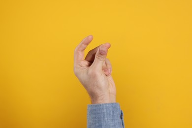 Man snapping fingers on yellow background, closeup of hand