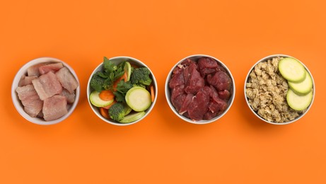 Feeding bowls with natural pet food on orange background, flat lay
