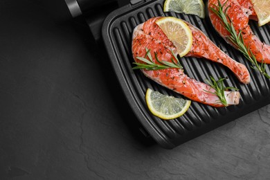Photo of Cooking salmon. Grill with fresh fish steaks, lemon and rosemary on dark table, top view. Space for text