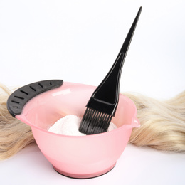 Strand of blond hair, bowl with dye and brush on white background