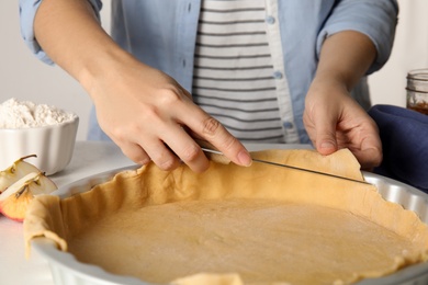 Woman cutting dough leftovers for traditional English apple pie in baking dish at table, closeup