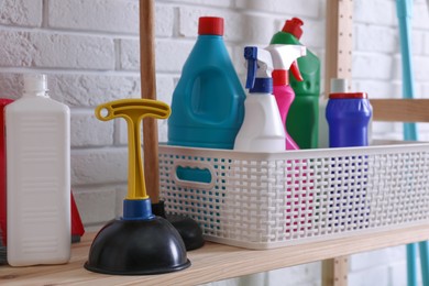 Plungers and basket with detergents on wooden shelf near white brick wall