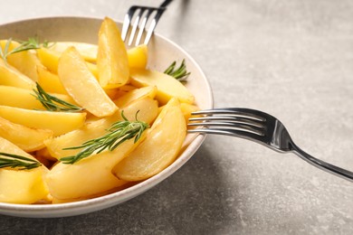 Plate with tasty baked potato wedges and rosemary on grey table, closeup
