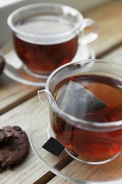 Photo of Bag of black tea in cups on wooden table indoors, closeup