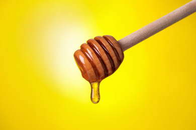 Dripping honey from dipper on yellow background, closeup