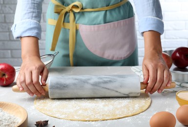 Woman rolling dough for apple pie at light grey table, closeup