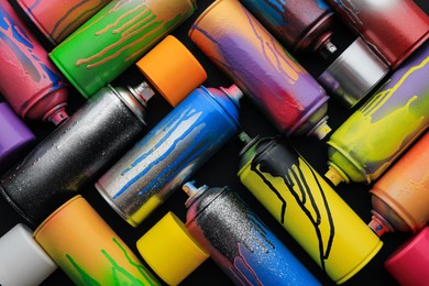 Photo of Used cans of spray paints on black background, flat lay. Graffiti supplies