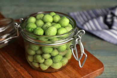 Tasty wasabi coated peanuts in glass jar on wooden table, closeup