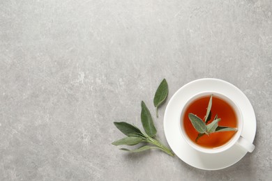 Cup of aromatic sage tea and fresh leaves on grey table, flat lay. Space for text